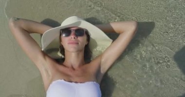 Beyaz yaz şapka ve sahilde deniz dalgaları ile yatan kadın video 