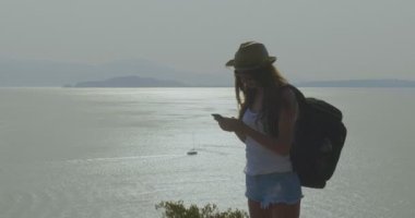 deniz manzaralı ve arka plan ufukta dağ tepe üzerinde duran cep telefonu tutan kadın video 