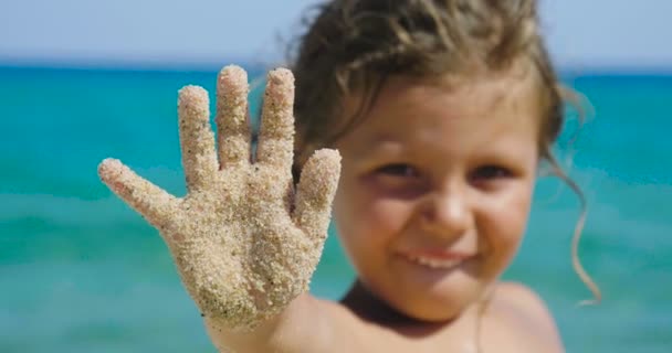 一个美丽的小女孩在沙滩上玩耍的肖像 可爱的微笑在太阳镜 背景的海黄色的沙子和蓝色的水 — 图库视频影像