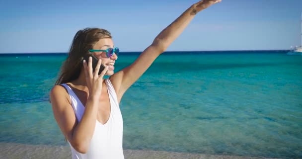 海で水の携帯電話で話していると メガネをかけて幸せな女のビデオ — ストック動画