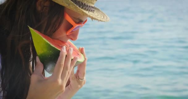 妇女戴帽子和太阳镜在蓝色的海洋吃新鲜的甜西瓜片的视频 — 图库视频影像