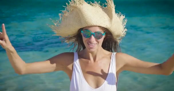 视频的妇女穿着白色夏季帽子在海水中 用手指显示舌头和片断标志 — 图库视频影像