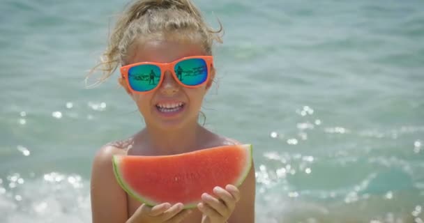 Holčička jí meloun na pláži se ochladit a v pozadí můžete vidět moře