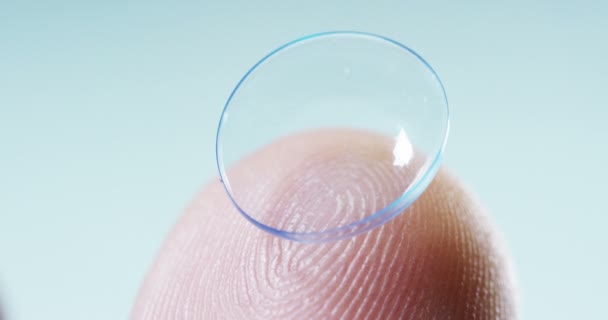 Video Van Transparante Oogcontact Lens Vinger Tegen Blauwe Achtergrond — Stockvideo