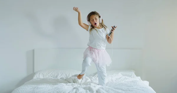 一个小女孩用耳机听音乐 在父母床上跳舞的肖像 — 图库照片