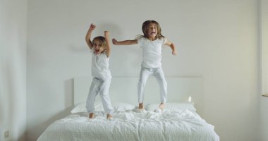 Beyaz pijama giymiş iki kız kardeş, yatağa atlamak ve eğlenin. Gençlik, sağlık ve sağlık, mutluluk ve Özgürlük kavramı.