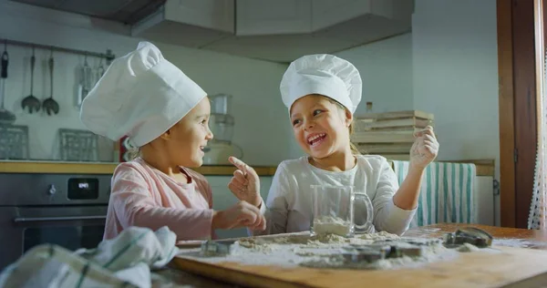 Two little girls in the kitchen prepare food, a dessert for the family. As they learn to cook they start playing with flour and smiling each other. Concept of: cooking classes, family, education.