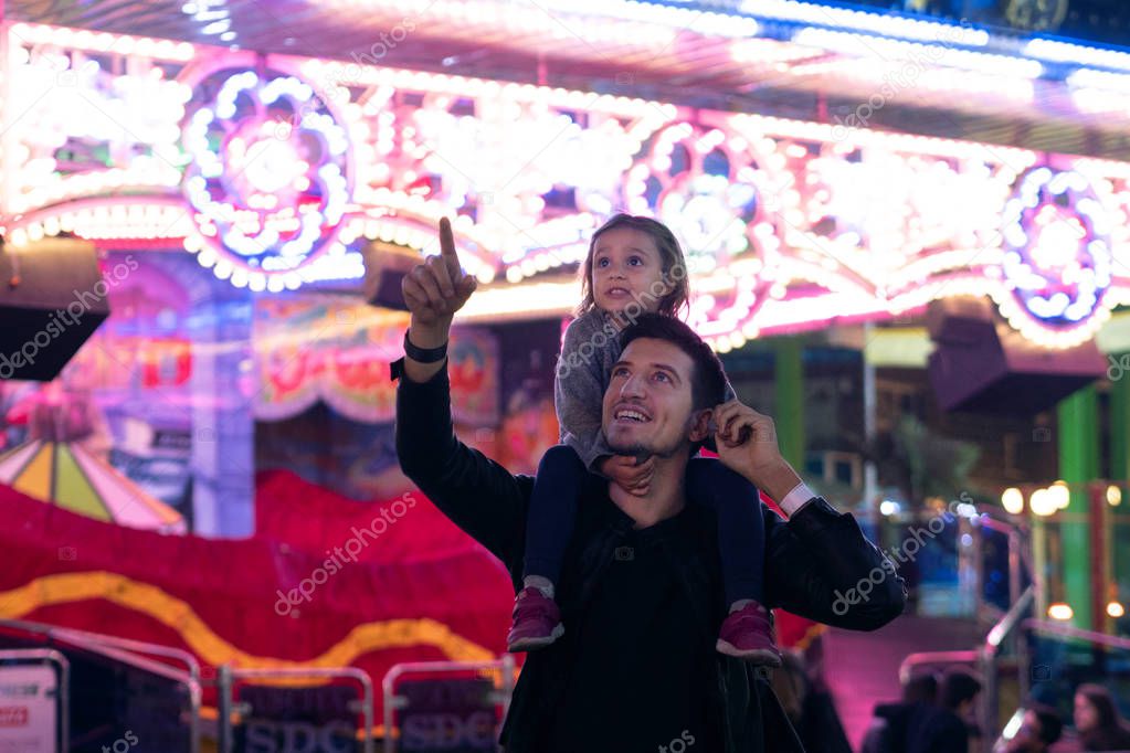 Portrait of a young father holding his  daughter on the enck  in  the Luna Park. Concept: Happiness, freedom, fun, family