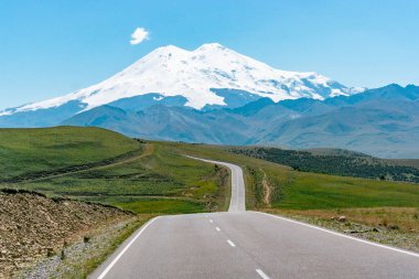 Avrupa 'nın en yüksek zirvesinin manzarası, güneşli bir yaz gününde yeşil tepeli Elbrus Dağı.