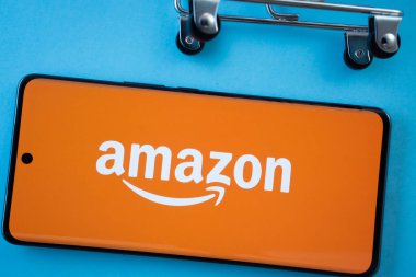 Dhaka, Bangladeş - 03 Temmuz 2025: Mavi arka planda alışveriş arabası tekerlekleri olan Amazon logosunu gösteren akıllı telefon ekranı.