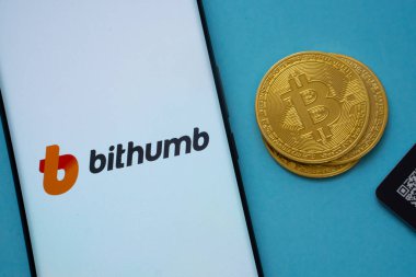 Dhaka, Bangladeş - 07 Mayıs 2025: Bitcoin yakınlarındaki akıllı telefon ekranında bithumb logosu ve mavi arkaplanda QR kodu.