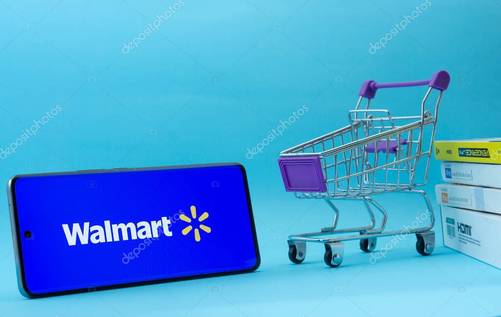 Dhaka, Bangladesh- 03 July 2025: Smartphone with Walmart logo next to a small shopping cart and boxes against a blue background.