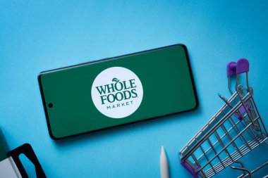 Dhaka, Bangladeş - 03 Temmuz 2025: Whole Foods Market logosunu mavi arka planda alışveriş arabasıyla gösteren akıllı telefon.