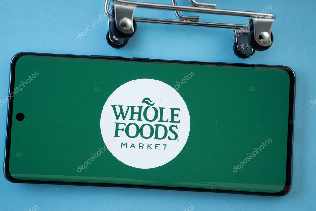 Dhaka, Bangladesh- 03 July 2025: Smartphone screen showing the Whole Foods Market logo with shopping cart wheels on a blue background.