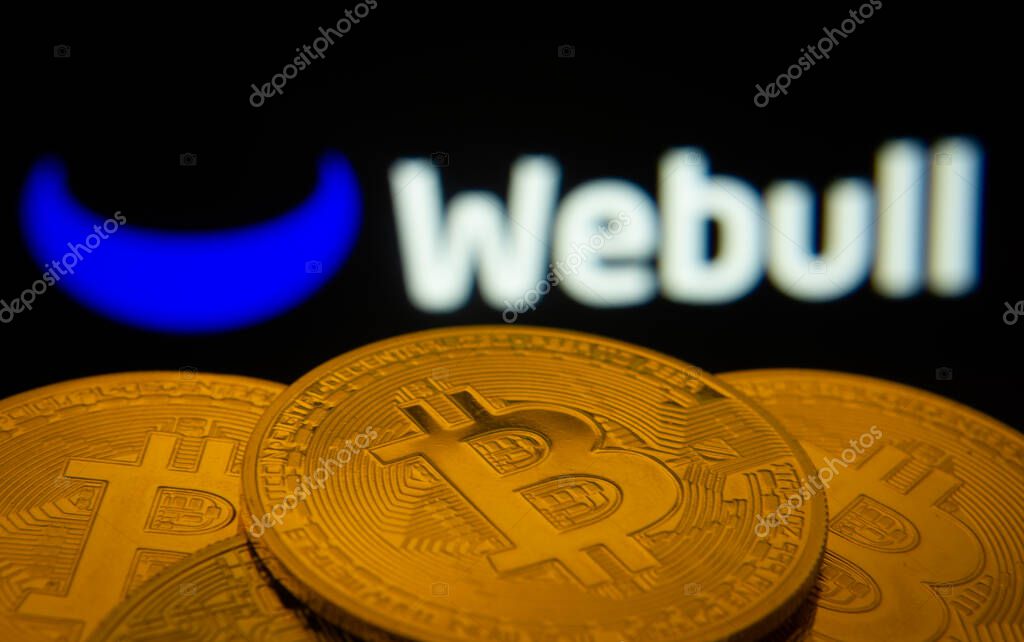 Dhaka, Bangladesh- 27 July 2025: Close-up of Bitcoin coins with the webull logo visible on a screen in the background.