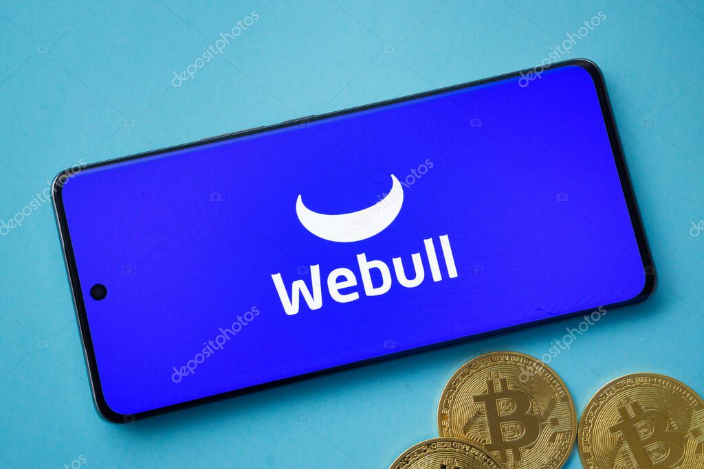 Dhaka, Bangladesh- 03 Sep 2025: webull logo on smartphone screen near Bitcoin coin and QR code on blue background.