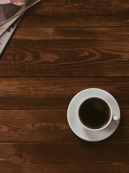 Xícara de café preto em uma mesa de madeira marrom com revista de moda. Processamento de autor, efeito de filme, tecla baixa . — Fotografia de Stock