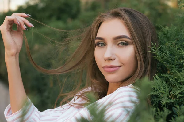 Menina atraente jovem perto do arbusto verde, tocando para o cabelo. Menina sorridente com cabelos longos, imagem com efeito de filme e processamento de autor . Fotografias De Stock Royalty-Free