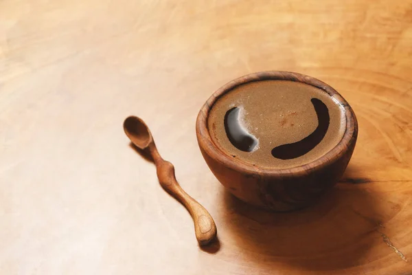 Ahşap arka plan üzerinde tahta kaşık ile ahşap fincan siyah kahve.