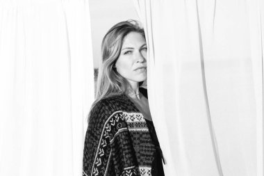 Beautiful young woman is looking to the camera, photo shoot with textile background on the meadow. End of summer, girl is happy and enjoying warm sunny day. Black and white color correction and stylish outfit matching to autumn colors