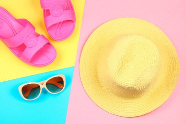 Şapka, güneş gözlüğü ve üç renkli terlik. Mavi, sarı ve pembe arka plan.