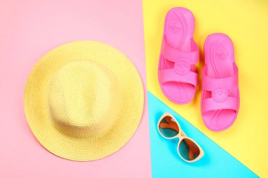Şapka, güneş gözlüğü ve üç renkli terlik. Mavi, sarı ve pembe arka plan.