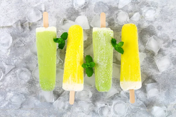 黄色和绿色水果冰淇淋在冰上的一根棍子在一盏灯桌上 — 图库照片