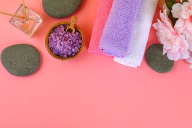 Spa pastel pembe bir arka plan üzerinde. Havlu, taş, aromamaslo, mor tuz banyosu ve pembe çiçekler