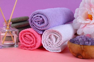 Spa pastel pembe bir arka plan üzerinde. Havlu, taş, aromamaslo, mor tuz banyosu ve pembe çiçekler