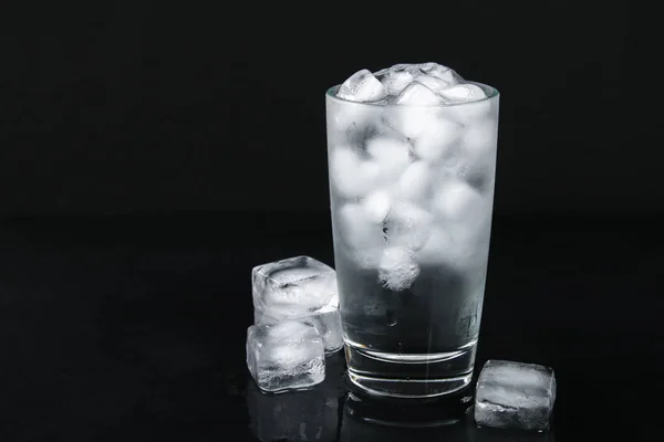 Ice water with ice and a leaf of mint and a straw in a glass on a black background