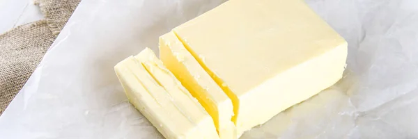 A bar of butter on a wooden board with a knife, on a white table. Ingredients for cooking