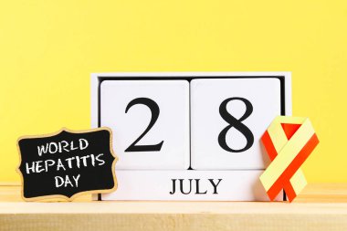 Dünya hepatit günü. Ahşap bir masa bir sarı duvar arka plan üzerinde Haziran 28 gösteren bir ahşap beyaz takvim. Kırmızı sarı şerit ve tebeşir tahtası