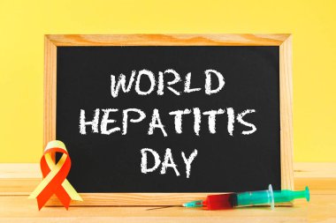 Metin dünya hepatit günü ile kara tahta. 28 Haziran'da. Kırmızı sarı bandın ve ahşap bir masa bir sarı duvar arka plan üzerinde kan şırınga