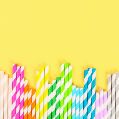 Çok renkli saman kağıt tüpler parlak sarı pastel arka plan üzerinde. Üstten görünüm, kopya alanı