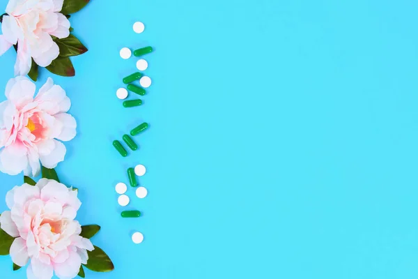 Capsules, pills and tablets with flowers on a blue table background. Top view, copy space, flat lay
