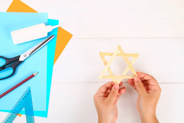 DIY. Davut'un Yıldızı dondurma dan elleriyle Beyaz ahşap bir masa üzerinde sopa