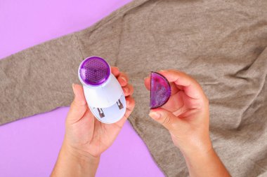 Tüysüz elinde kaldırmak için bir makine. Kazak ile Mor pastel arka plan üzerinde bobble