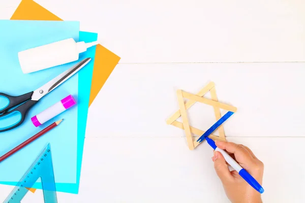 DIY. Davut'un Yıldızı dondurma dan elleriyle Beyaz ahşap bir masa üzerinde sopa