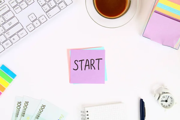 Text Start on the sticker note on the white desktop next to the coffee mug and the keyboard. Top view, flat layout