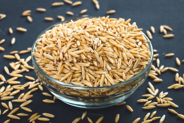 Gri bir tablo üzerinde bir cam kapta yulaf çiğ tanesi