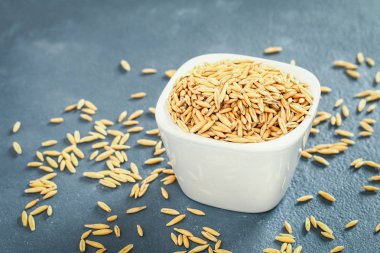 Gri bir tablo üzerinde bir beyaz cam kapta yulaf çiğ tanesi