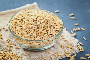 Gri bir tablo üzerinde bir cam kapta yulaf çiğ tanesi