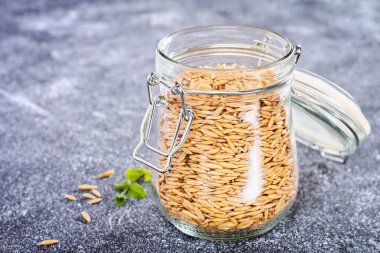 Çiğ yulaf taneleri gri bir tablo üzerinde cam kavanozda