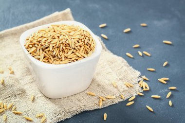 Gri bir tablo üzerinde bir beyaz cam kapta yulaf çiğ tanesi