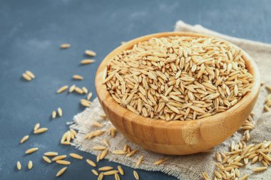 Gri bir tablo üzerinde ahşap bir kase yulaf çiğ tanesi