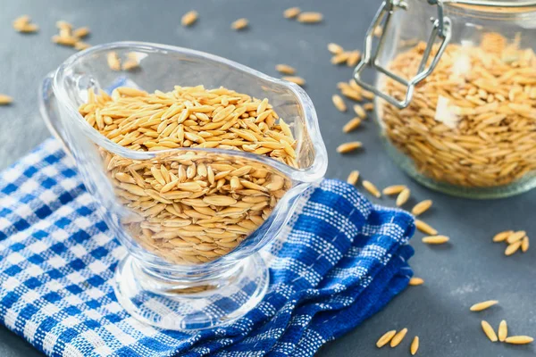 Gri bir tablo üzerinde bir cam kapta çiğ yulaf taneleri