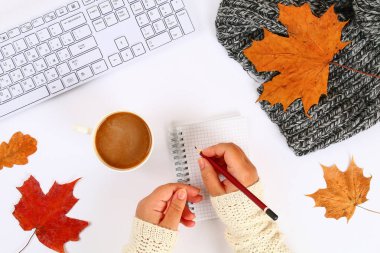 Hatmi bir boş blok ve klavye yanında beyaz bir masaüstünde elinde kahveyle, sonbahar yaprakları. Sonbahar ruh. Üstten görünüm, düz düzen. Kopyalama alanı