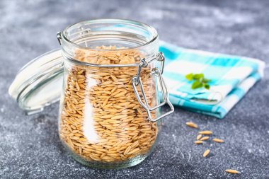 Çiğ yulaf taneleri gri bir tablo üzerinde cam kavanozda