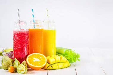 Mango, portakal, muz, kereviz, çilek, ahşap bir masa üzerinde şişelerde çok renkli smoothies
