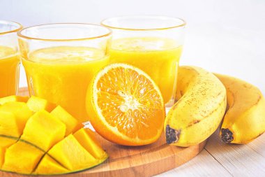 Mango, muz ve portakal Beyaz ahşap bir masa üzerinde sarı güler yüzlü